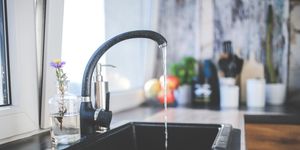 A modern kitchen sink with running water, a sleek faucet, and a vase on the countertop.