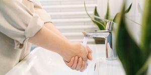 Close-up of hands washing under a modern faucet with indoor plants nearby.